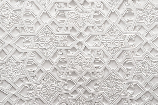 White carved plaster wall with geometric and floral patterns inside Muhammad Amin Khan Madrasa in Khiva. Intricate Islamic ornamental relief ideal for architectural and cultural design projects.