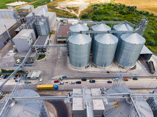Storage silos and grain processing facility located near a rural area, showing transportation and processing activities during daytime © DSMT