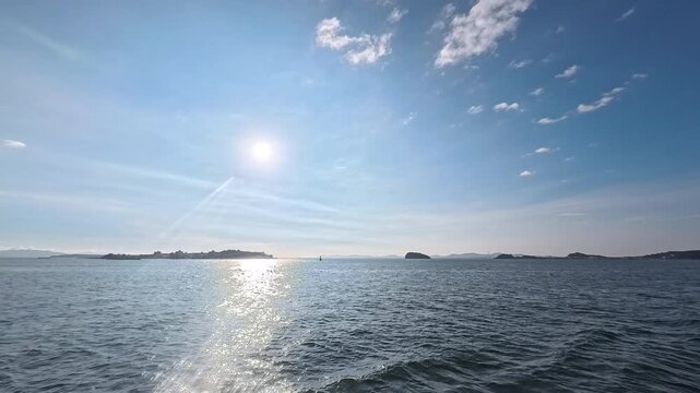 Cinematic real-time video of glowing sun path on calm ocean surface with scenic island backdrop