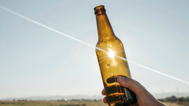 Hand Holding Bottle with Sunlight and Clear Sky, Refreshing Beverage Concept