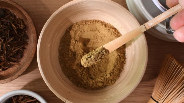 Person scoops roasted hojicha powder with bamboo spoon and presents its fine texture during traditional tea preparation.