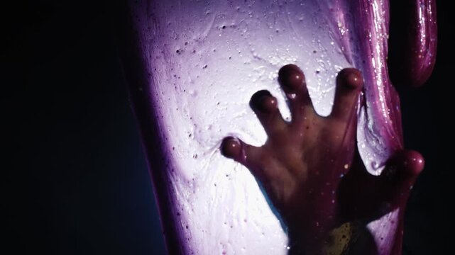 Silhouette of hand trapped behind purple slime film in dark cinematic scene.