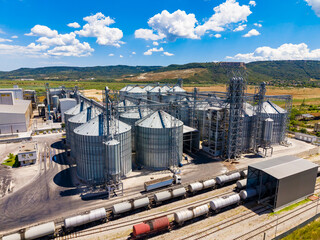 Large grain storage facility with silos and train tracks near a rural area on a sunny day © DSMT