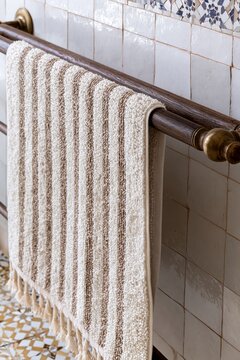 Hand-woven cotton striped towel in warm cream and dusty ochre draped over a dark teak rail in a Moroccan riad bathroom setting