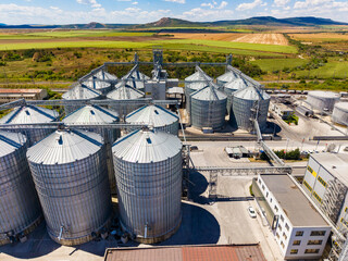 Large silos stand in a field near a factory with green hills in the background on a sunny day © DSMT
