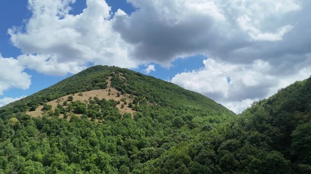 Montagna ricoperta da vegetazione verde con foresta fitta, pendii naturali e cielo parzialmente nuvoloso