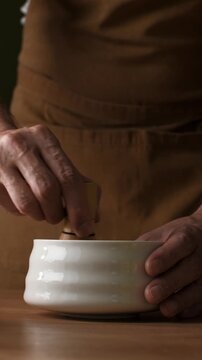 Hands whisk roasted hojicha powder with bamboo chasen in ceramic bowl to make smooth tea during Japanese preparation ritual.