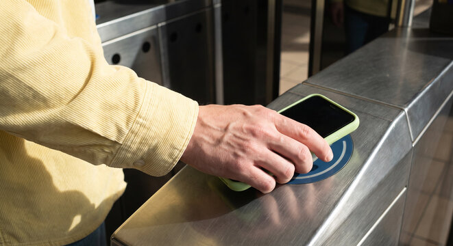 A commuter taps a smartphone on a contactless reader at a transit turnstile, showcasing mobile payment, touchless ticketing, and urban commuting in a busy public transport station