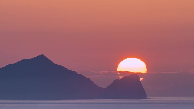 Breathtaking view of the morning sun rising directly behind the peak of Turtle Island in Yilan, Taiwan, casting a warm orange glow over the ocean.