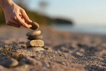 Fototapete Beruhigend Hand stacks stones on a sandy beach, creating balance as the sea fades in the background, a calm lifestyle moment focused on mindfulness and nature  © SHOTPRIME STUDIO