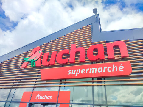 Colleville, France - June 28, 2026: Auchan supermarket facade with large red sign and wooden slats under blue sky, modern retail architecture