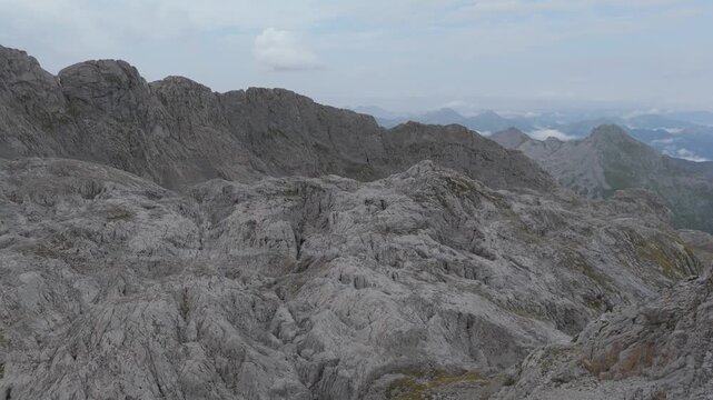 Aerial drone pan left shot over the rugged, rocky landscape of Garita Bajera mountain in Picos de Europa, Asturias, Spain. High peaks and cliffs under a cloudy sky.