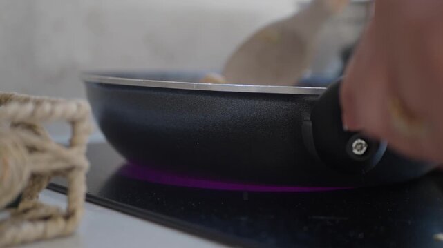 A person skillfully flipping and mixing food in a frying pan on an induction stove, showcasing dynamic cooking action and culinary motion in a home kitchen setting