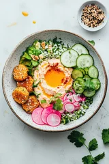 Vibrant plant-based meal bowl featuring creamy hummus, golden falafel, sliced cucumber, bright radishes, green avocado, and fluffy cauliflower rice. © Tetiana