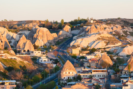 Goreme village lies among volcanic rock formations in Cappadocia Turkey during early morning light. Goreme roads wind between carved dwellings, hills, and distinctive landscape under clear sky