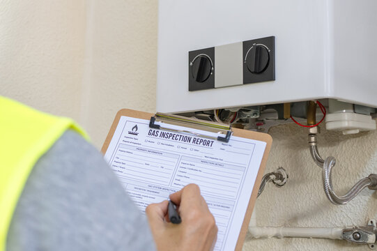 Gas technician inspecting a residential water heater and completing a safety inspection report on a clipboard during routine home maintenance and annual gas service