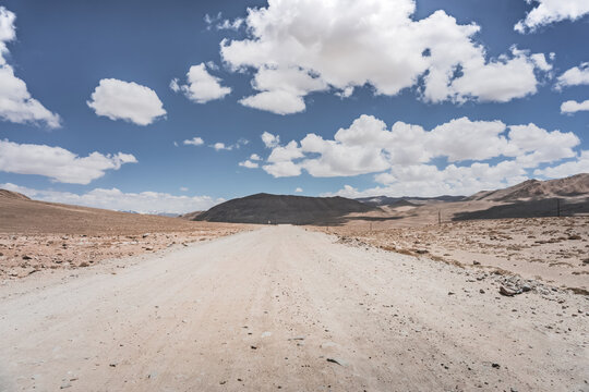 Dusty road of the Pamir Highway winds and twists in the valley of the Tien Shan mountains in Tajikistan in Pamir, landscape in the high desert mountains for background