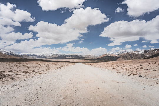 Dusty road of the Pamir Highway winds and twists in the valley of the Tien Shan mountains in Tajikistan in Pamir, landscape in the high desert mountains for background