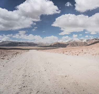 Dusty road of the Pamir Highway winds and twists in the valley of the Tien Shan mountains in Tajikistan in Pamir, landscape in the high desert mountains for background