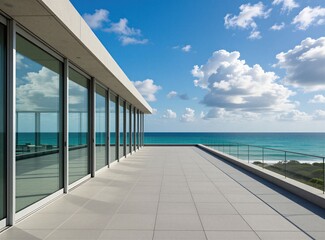 Obraz premium Modern minimalist terrace building exterior near blue ocean. Large glass windows reflect sky clouds. Sunny day bright light illuminates white stone floor tiles. Empty luxury house balcony provides
