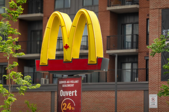 Montreal, Quebec, Canada. July 30, 2026. Iconic McDonald's Golden Arches sign with maple leaf in front of brick residential building.