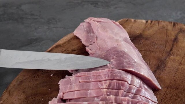 Slicing Cooked Ham - A white man slicing cooked pork ham on a wooden cutting board
