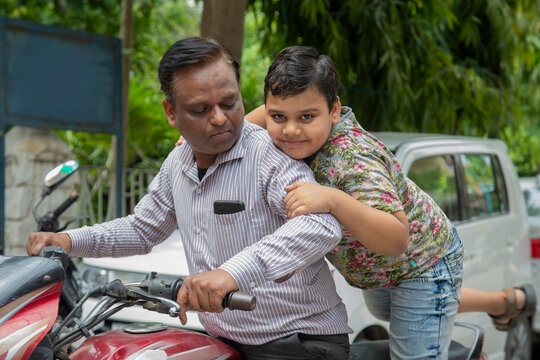 young boy trying to sit on a bike with his father