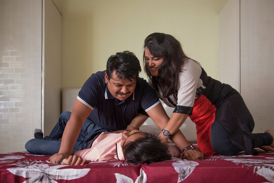 Husband and wife tickling their son on bed at home 