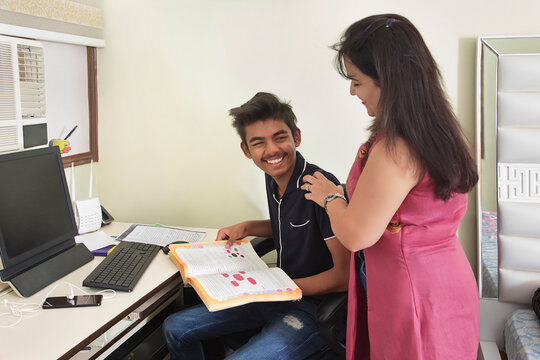 Mother helping her son in studying for exams at home 