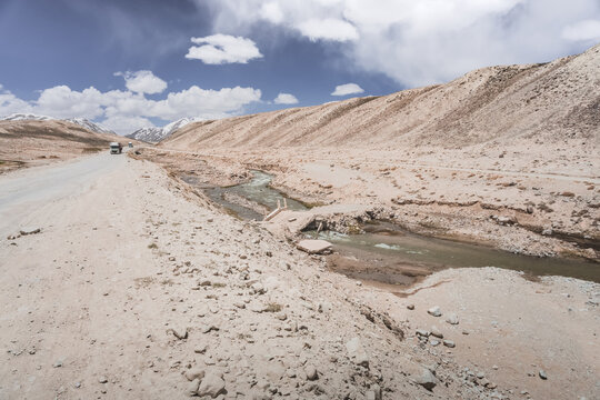 The Pamir Highway and a destroyed road bridge over a mountain river A dusty road with trucks. The hot, high altitude of Tajikistan's Tien Shan Mountains makes transportation difficult