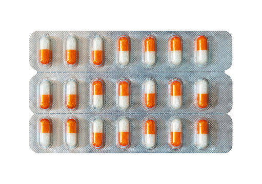 Blister pack with orange and white capsules on gray background.