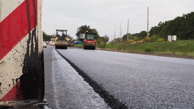 Road rollers compacting fresh asphalt during highway repair and construction with traffic cone in the foreground