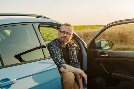 Pensive mature male driver taking a break and relaxing in vehicle during road trip at sundown. Side view.