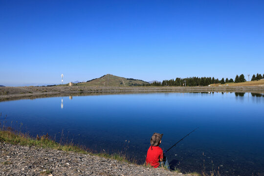 Jeune gar&ccedil;on p&ecirc;chant au bord d'un petit lac de montagne. Col de la L&eacute;zette. Les Saisies - Beaufortain - Savoie