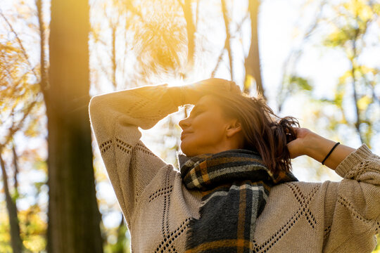 Mature Caucasian woman in warm sweater and scarf enjoying fresh air in autumn forest. Mental health and healthy aging concept