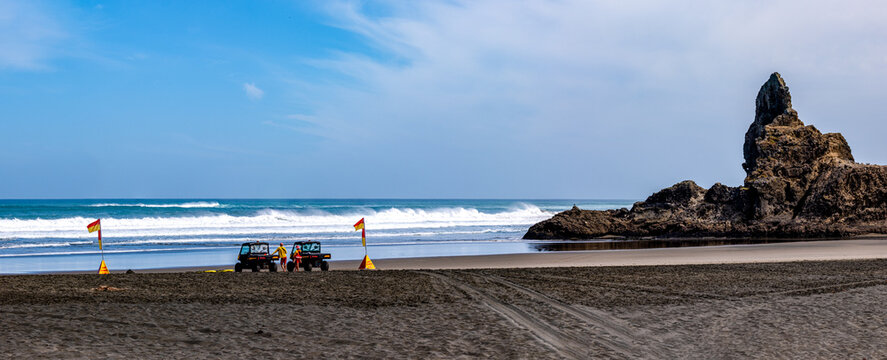 Baderettung am Piha Beach mit Lifeguards, Rettungsfahrzeugen und Camel Rock, Waitakere Ranges, Auckland, Neuseeland