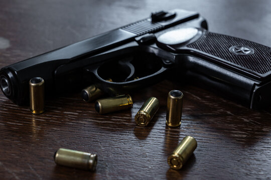 Black handgun lying on dark textured wooden surface with scattered non lethal ammunition cartridges containing black rubber bullets.