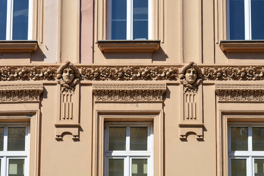 Decorative face sculptures and floral relief horizontal bands adorn the beige facade of a historic European building between rows of classic windows