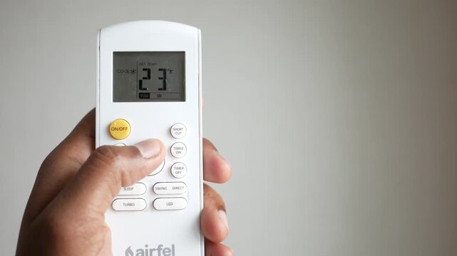 Person increasing temperature on white air conditioner remote control unit with digital display