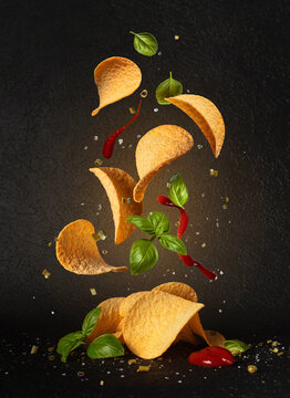 Flying potato chips with tomato sauce and fresh basil leaves. Food levitation concept on black background
