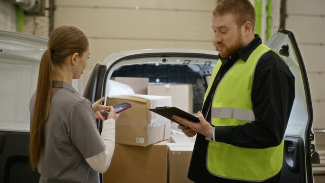 Young adult Caucasian female worker taking photo of cargo and signing delivery document on clipboard held by male courier near van. Perfect for logistics and e-commerce supply chain marketing