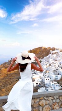 A tourist woman in a white dress looks at the beautiful view of the town at Serifos island, Cyclades, Greece, during sunset time