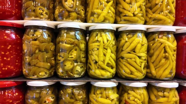 Shelves of assorted pickled peppers and chili pastes in glass jars for sale at market