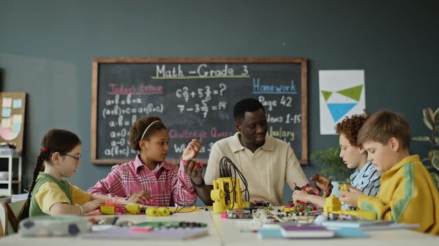 African American male teacher guiding multiethnic children during robotics class in elementary school. Video is suitable for promoting STEM education programs and modern school curricular