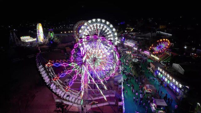Aerial night view of illuminated Ferris wheels and amusement park rides at a local fair ground