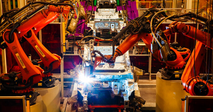 Robotic arms are welding car frames on the production line at a car factory.