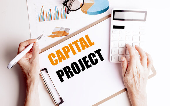 Capital project concept with hands using calculator near clipboard with financial charts and business documents