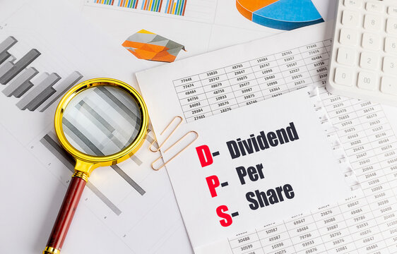 Dividend per share dps acronym on financial documents with magnifying glass and calculator