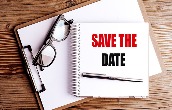 Save the date text on notebook with pen, glasses and clipboard on wooden desk background