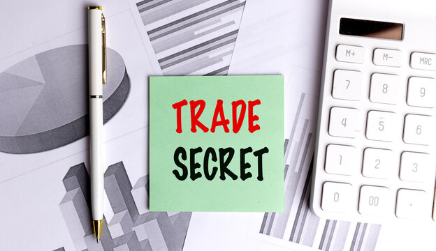 Trade secret concept with sticky note, calculator, pen and financial charts on office desk background